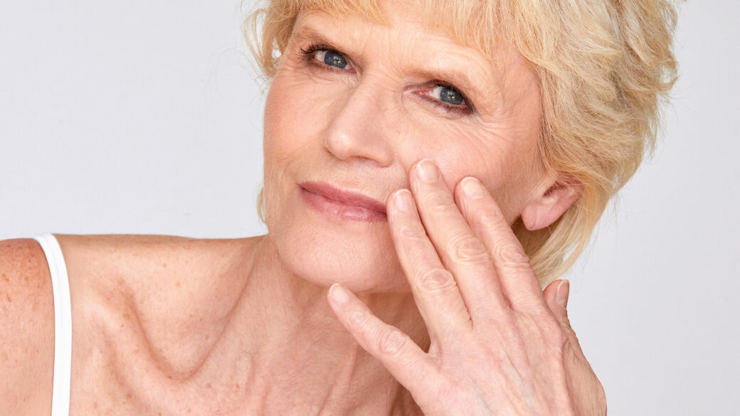 Mature woman gently touching her cheek while assessing facial skin quality.