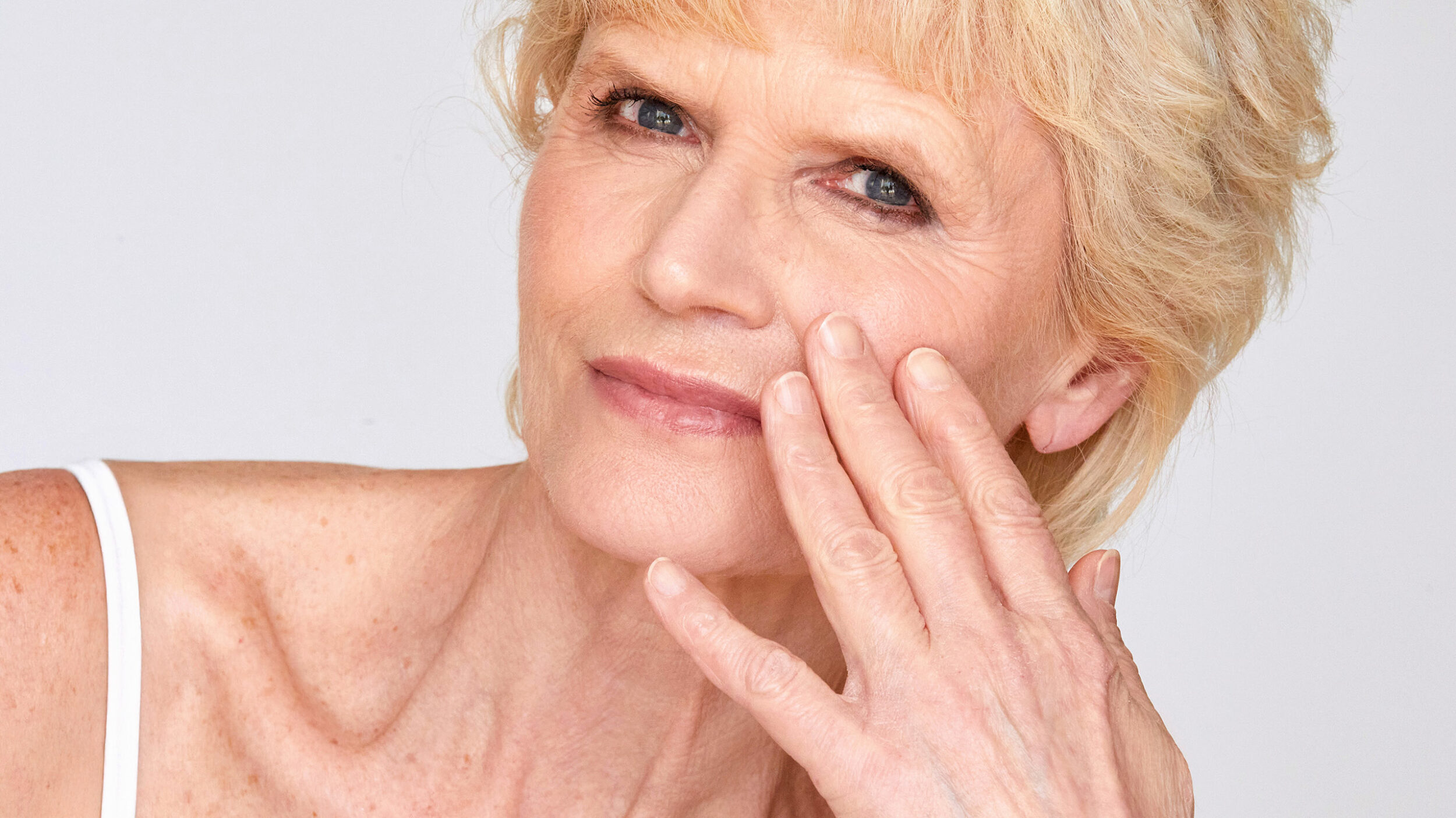 Mature woman gently touching her cheek while assessing facial skin quality.