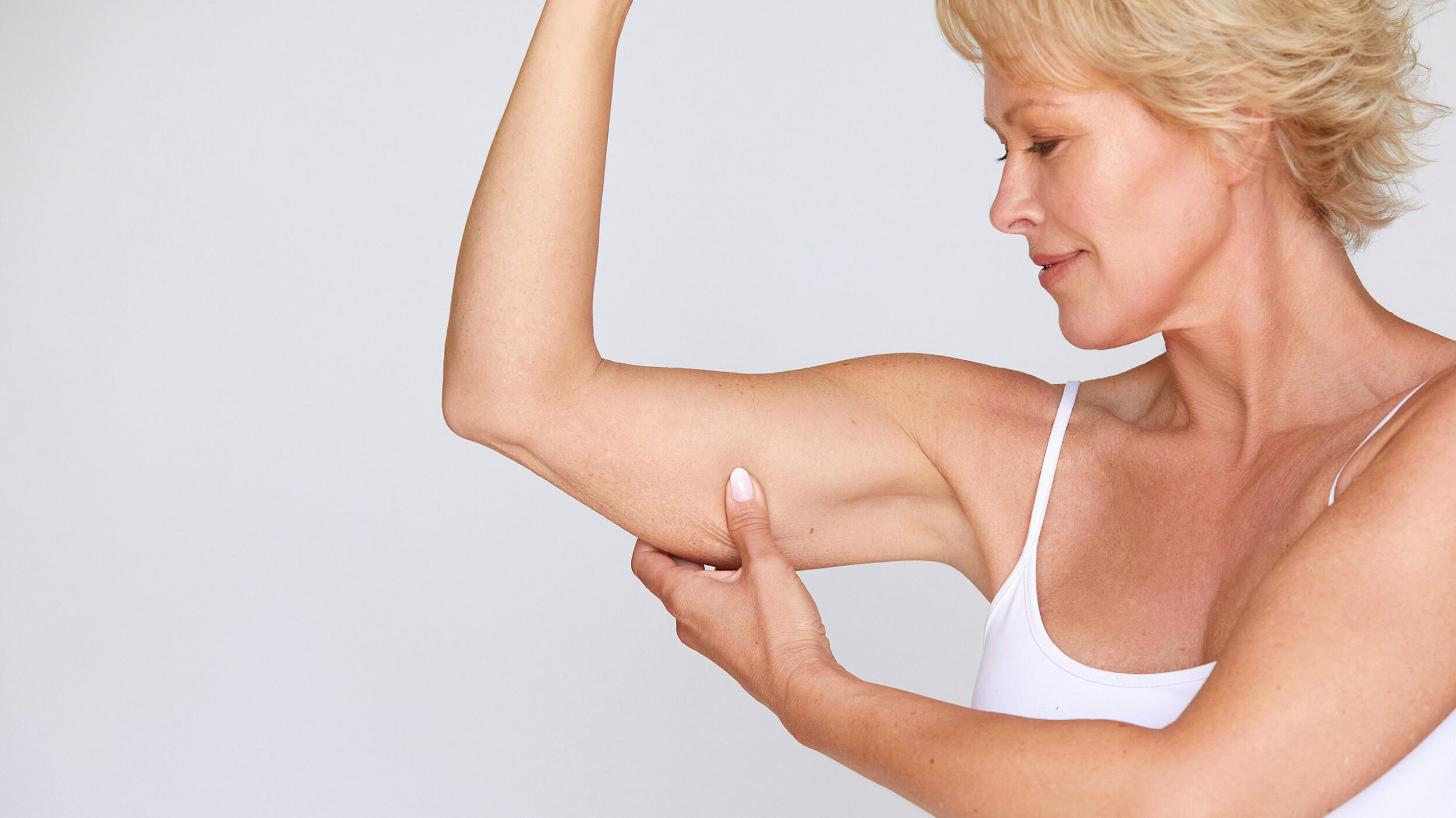 Woman examining the skin on her upper arm before aesthetic arm rejuvenation treatment.