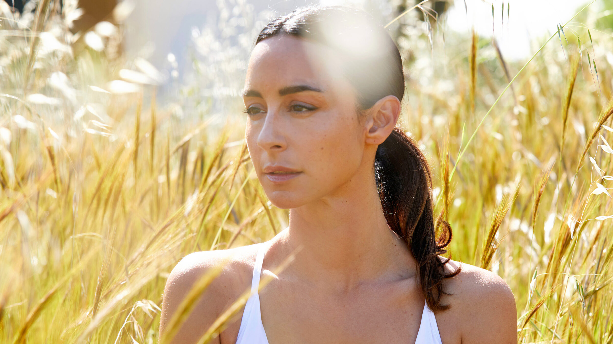 Woman standing in a sunlit field representing sustainability and natural skin health.