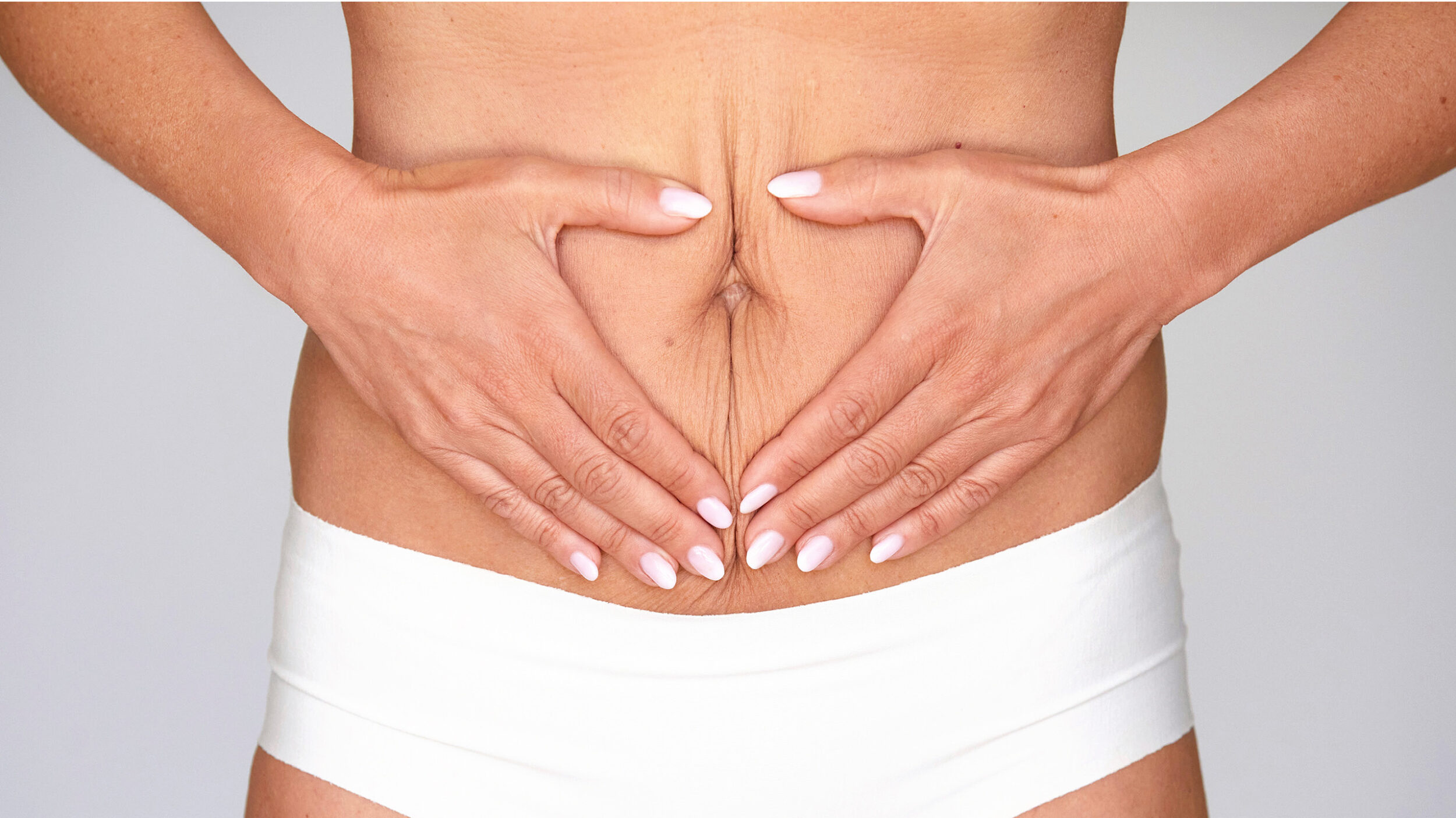 Woman holding the lower abdomen after abdominal skin tightening treatment.